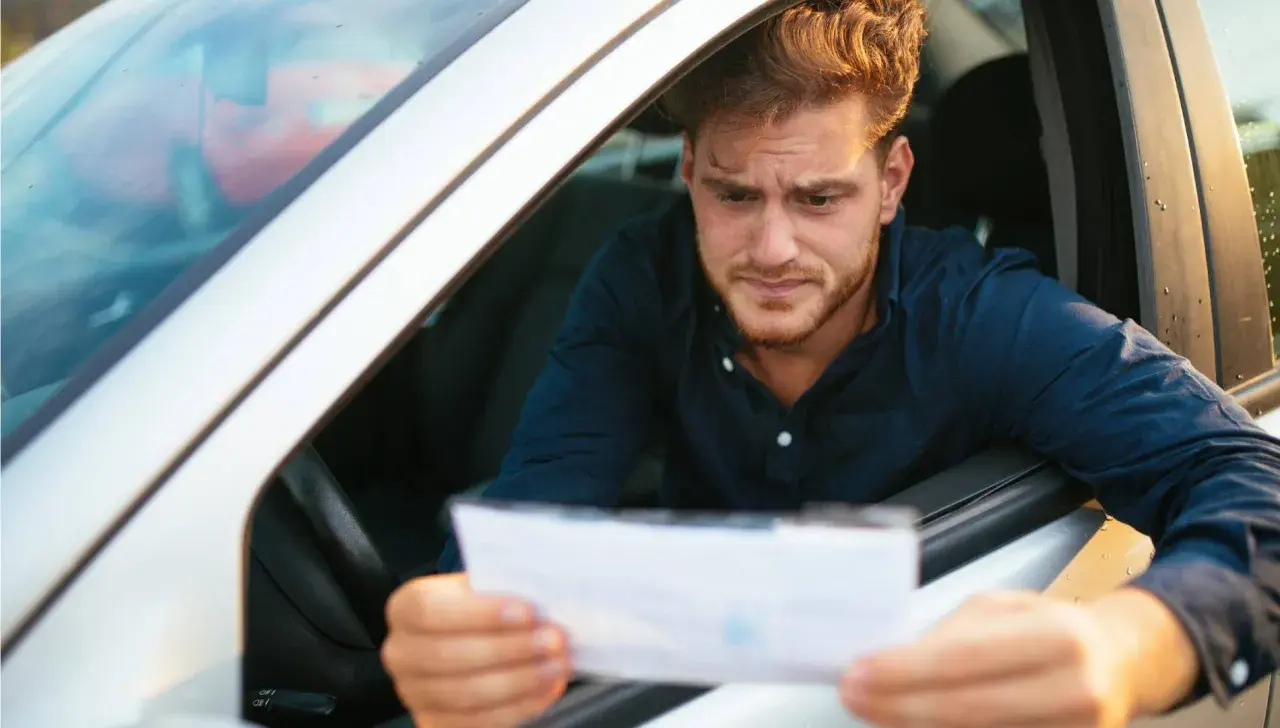 Hombre preocupado en su coche, mirando un papel que podría ser una multa. Se pregunta cuánto tarda en llegar una multa.