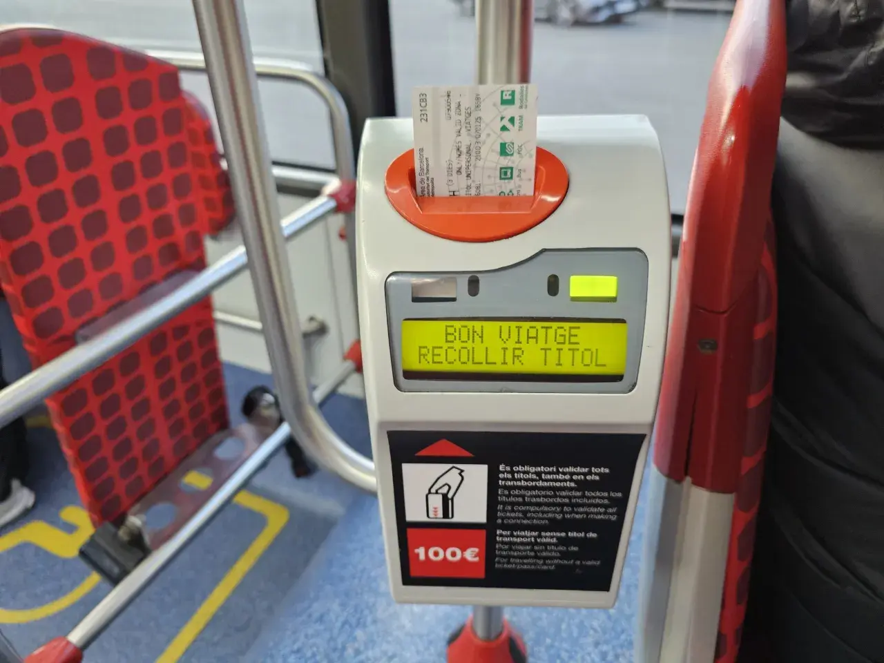 Validando billete para prendre le bus a Barcelone. Asientos rojos con patrón de cuadros en el interior del autobús.