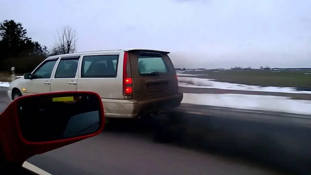 Un coche emite una densa nube de humo negro mientras circula por una carretera nevada.