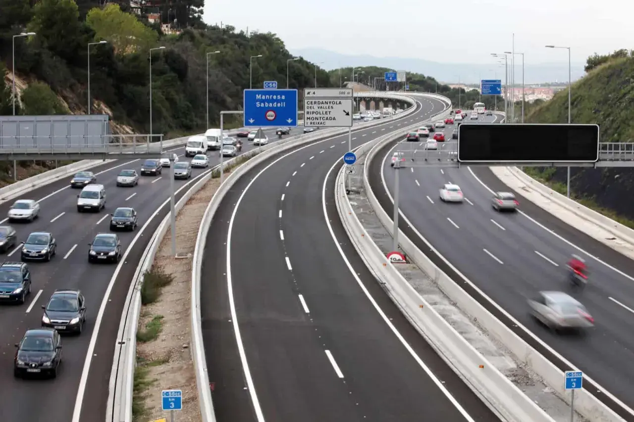 Autopista con varios carriles, incluyendo un carril Vao, con tráfico de coches y furgonetas. Señales de tráfico indican direcciones.