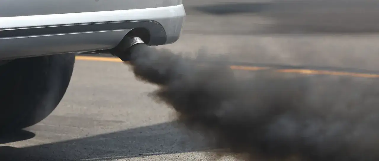 Un coche emite una densa nube de humo negro por el tubo de escape, contaminando el aire.