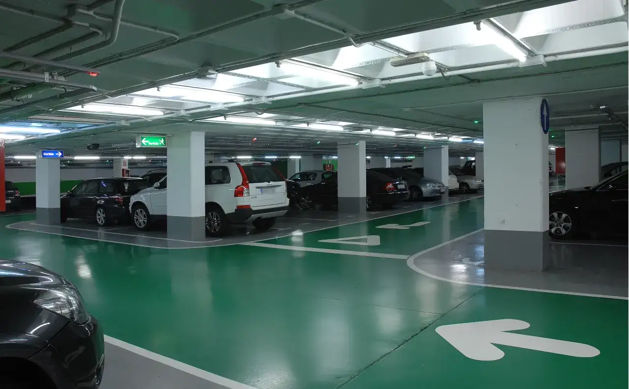 Estacionamiento subterr&aacute;neo con coches, se&ntilde;alizaci&oacute;n de salida y flechas en el suelo. El bsm flos i calcat indica la direcci&oacute;n.