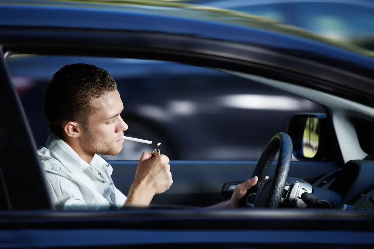 Joven enciende un cigarrillo mientras conduce. Se puede fumar conduciendo, pero con precauci&oacute;n.