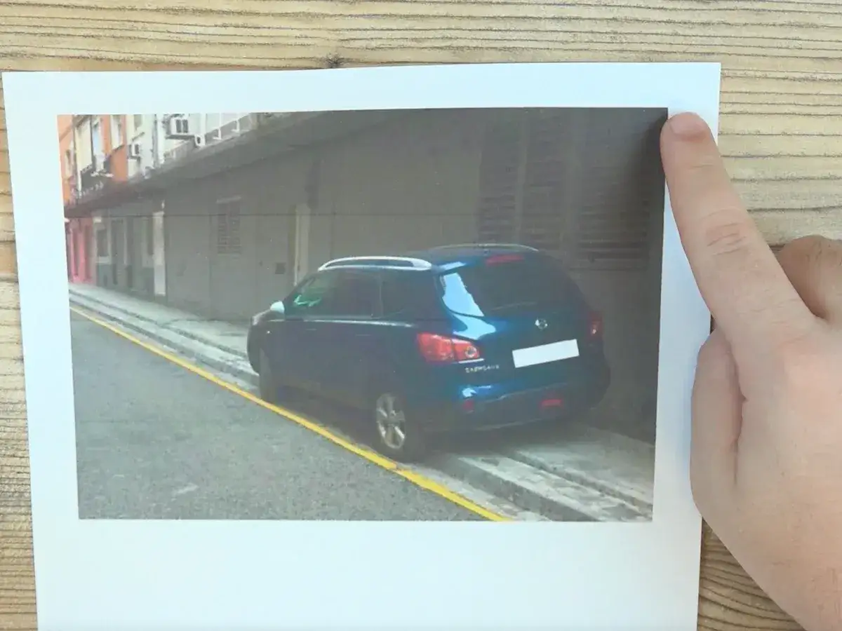 Un coche azul aparcado en una zona con l&iacute;nea amarilla, probablemente recibiendo una multa por aparcar mal.