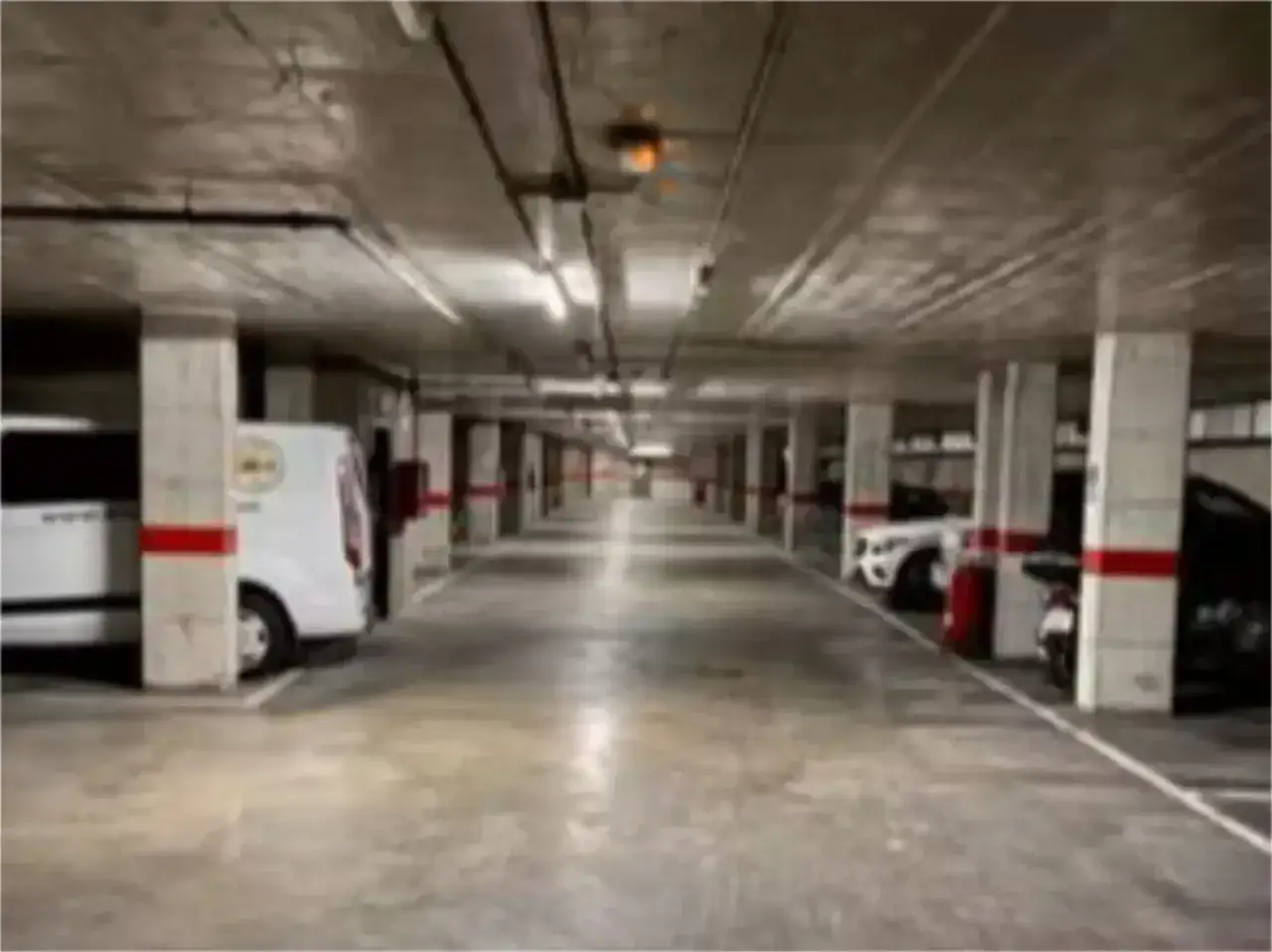 Pasillo de aparcamiento subterr&aacute;neo con coches y furgonetas. L&iacute;neas blancas marcan las plazas, algunas en diagonal. Hay parking gratis disponible.