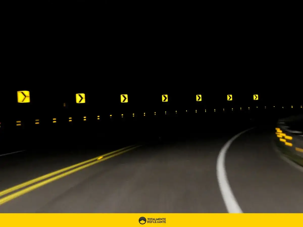Curva nocturna señalizada con flechas amarillas y puntos reflectantes. El catadióptrico guía el camino.