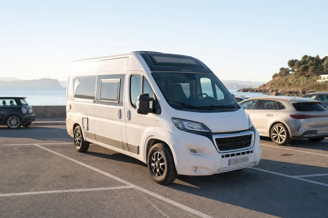 Una autocaravana blanca aparcada en un parking junto al mar. Las autocaravanas pueden aparcar en cualquier sitio, ofreciendo libertad para explorar.