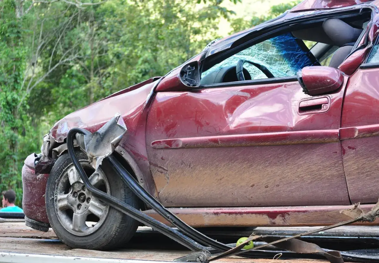 Coche rojo con siniestro total, chasis deformado, parabrisas roto y suciedad.