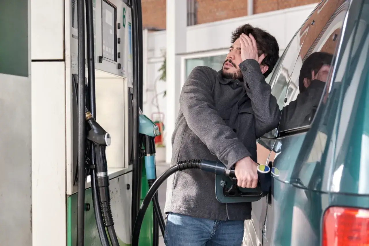 Hombre preocupado intenta echar gasolina a un coche di&eacute;sel, con la mano en la cabeza y la manguera de la gasolinera en la otra.