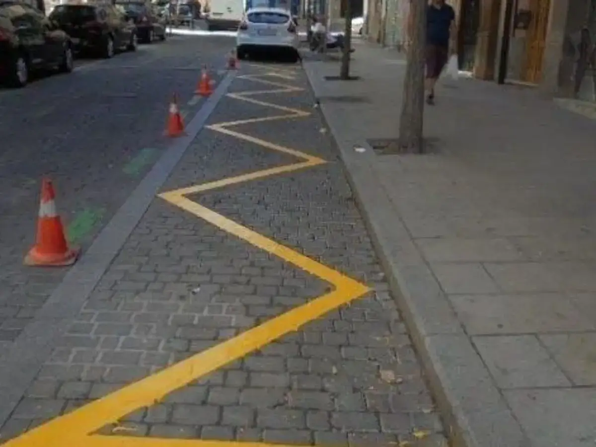 Zigzag amarillo marca la zona amarilla de Barcelona. Conos naranjas y coches aparcados en la calle empedrada.