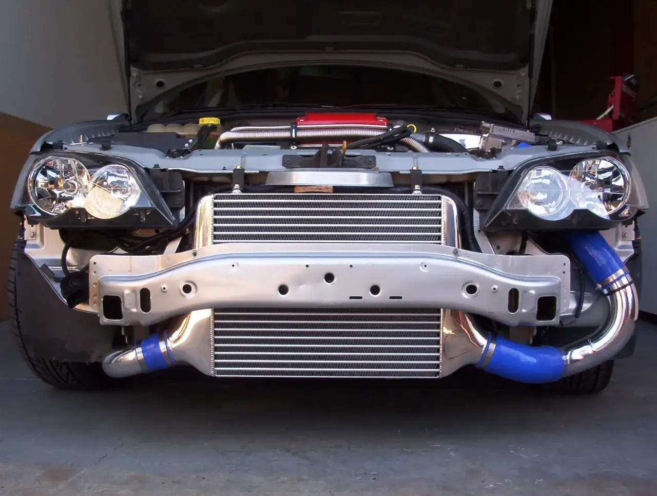 El intercooler que es un componente clave para mejorar el rendimiento del motor, se ve instalado en la parte frontal de un coche, con sus tubos azules conectados.