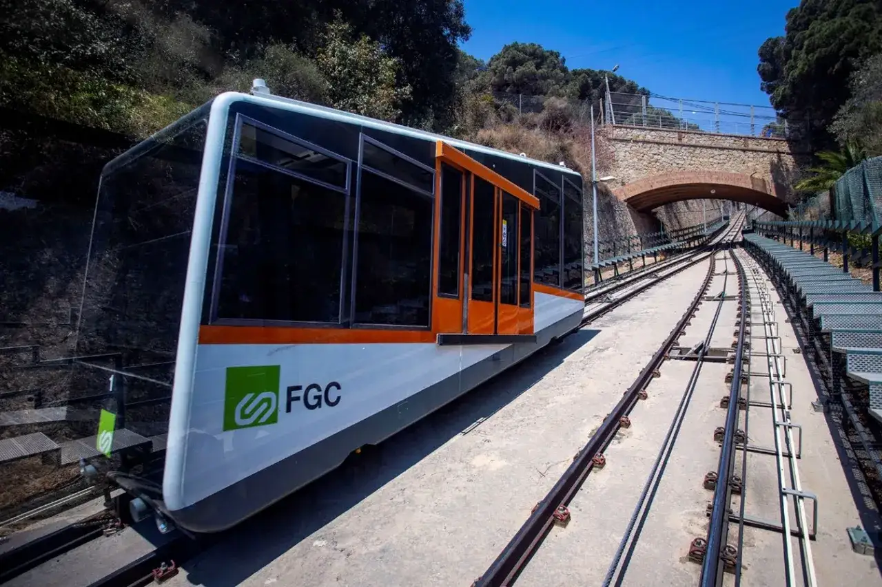 El funicular de Vallvidrera asciende por la ladera, con su moderno vag&oacute;n blanco y naranja listo para el viaje.