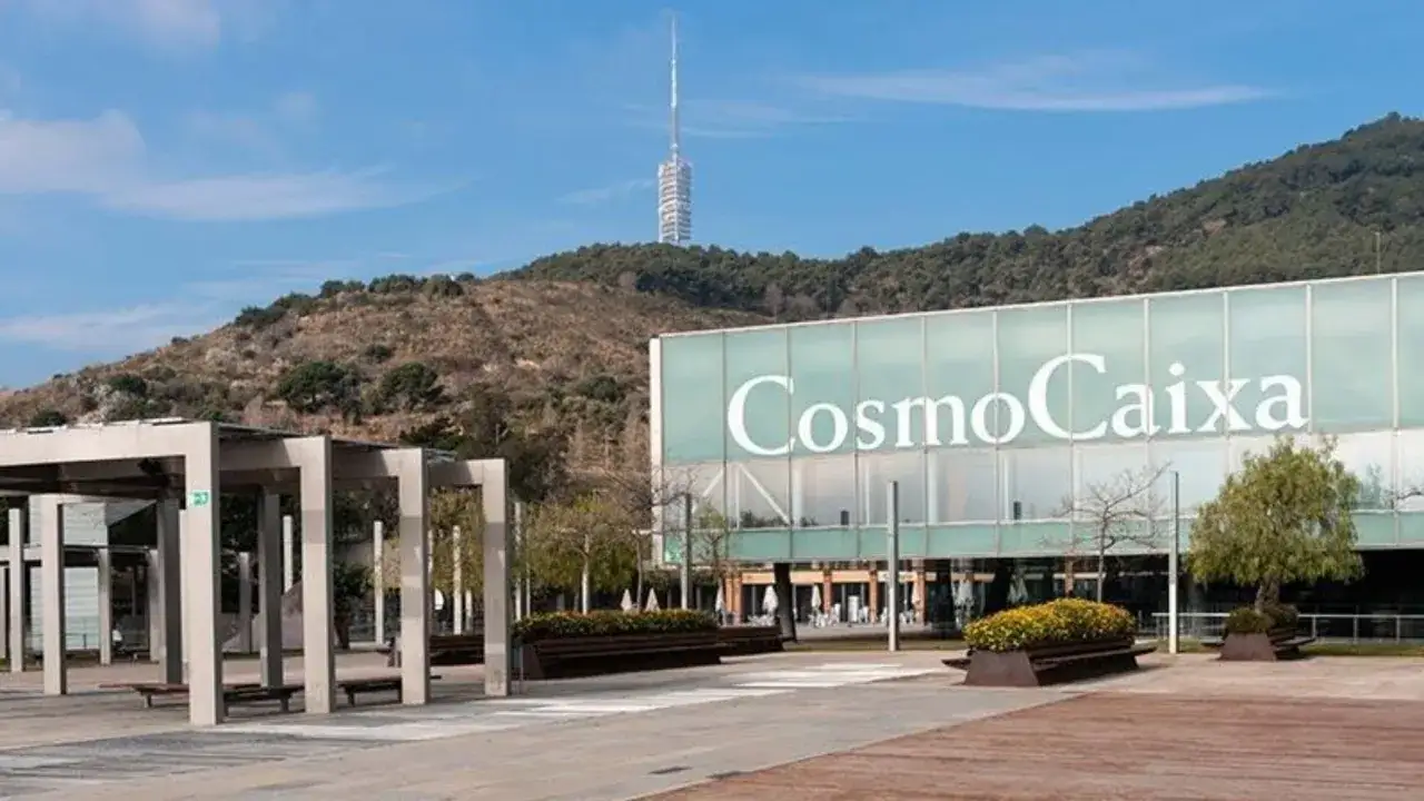 Edificio CosmoCaixa con su cartel luminoso. Al fondo, la montaña de Montjuïc y la Torre de Comunicaciones. Zona de bancos y pérgolas, ideal para el cosmocaixa parking.