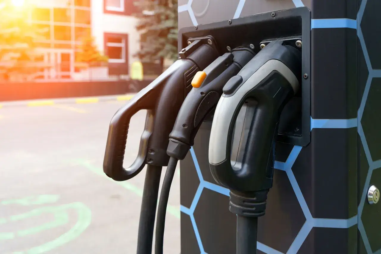Tres cables de carga para veh&iacute;culos el&eacute;ctricos cuelgan de una estaci&oacute;n. Estos puntos de recarga son esenciales para la movilidad sostenible.