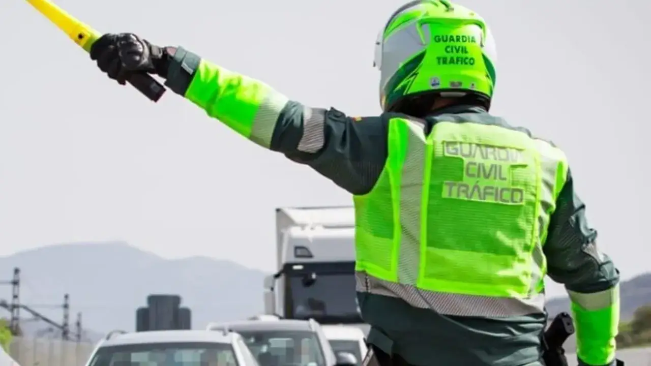 Agente de la Guardia Civil de Tr&aacute;fico, con chaleco reflectante y casco, dirige el tr&aacute;fico con una se&ntilde;al luminosa.