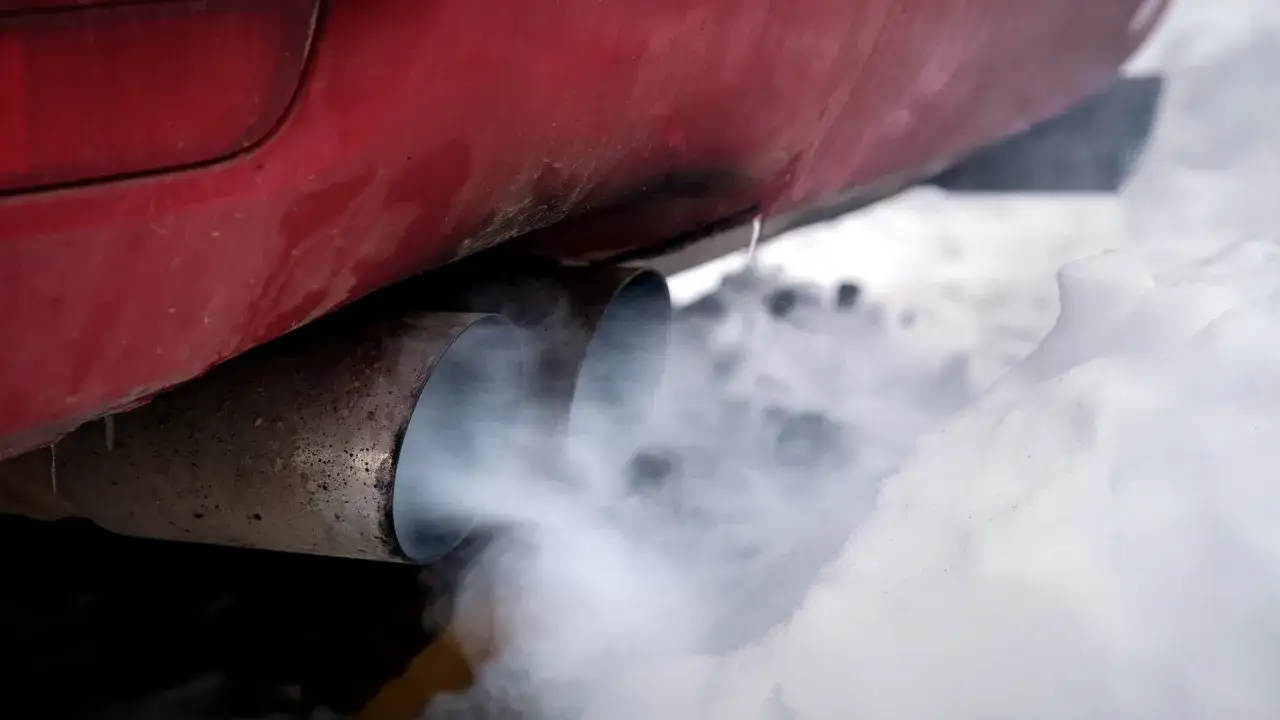 El coche echa humo blanco y huele a quemado. El tubo de escape expulsa vapor denso sobre la nieve.