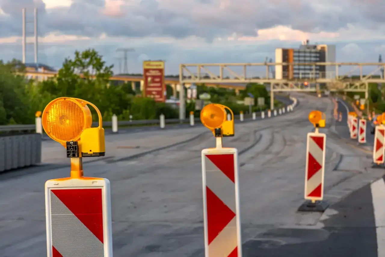Una hilera de postes con luces naranjas y franjas rojas y blancas, una señal de balizamiento, marca el camino en una carretera en construcción.